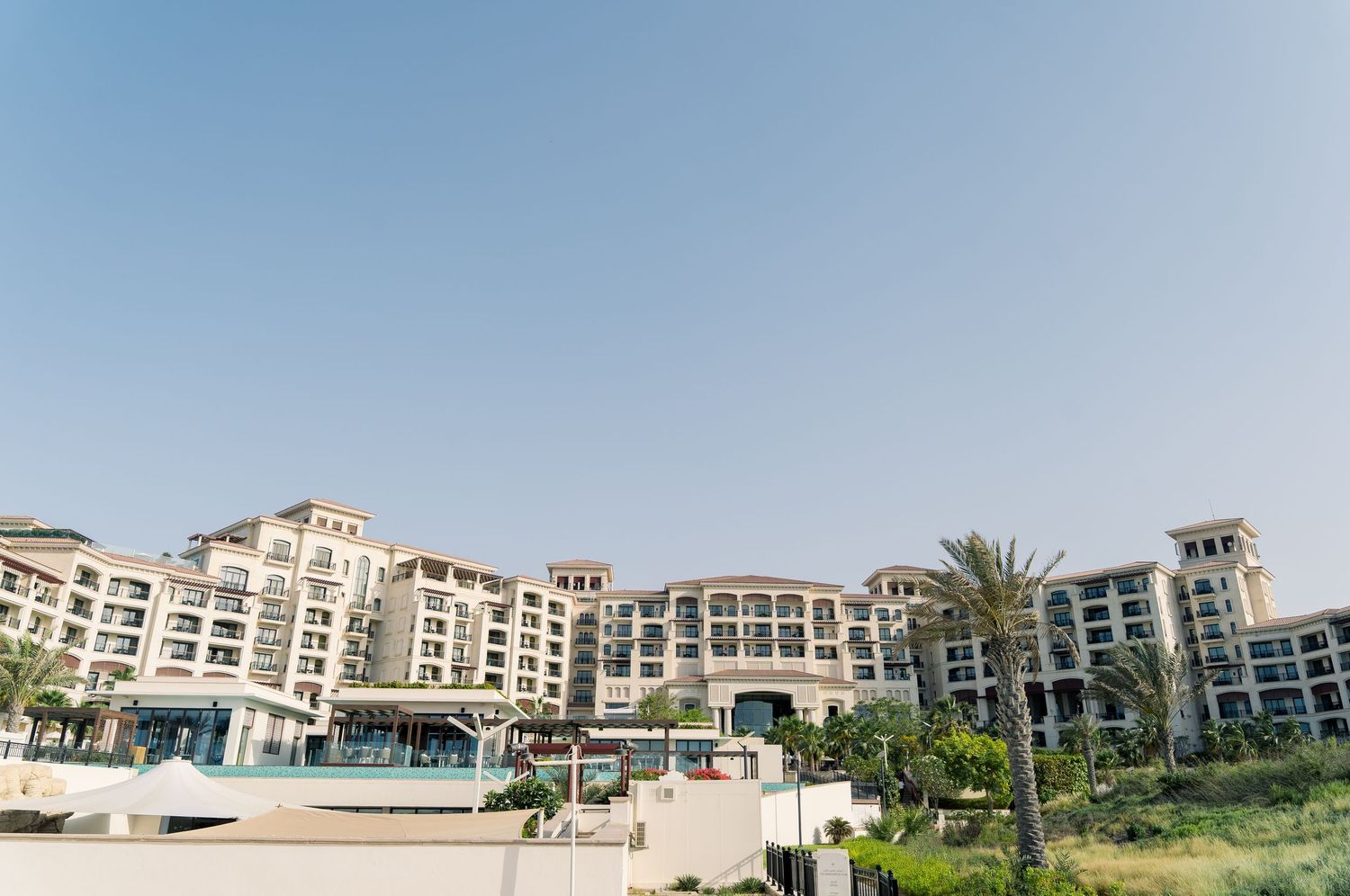 Luxurious beachfront resort with Mediterranean-style architecture and palm trees against a clear blue sky.