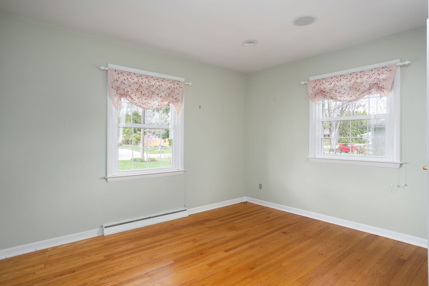 Bedroom with hardwood floors, mint green walls, and floral valances over double windows.