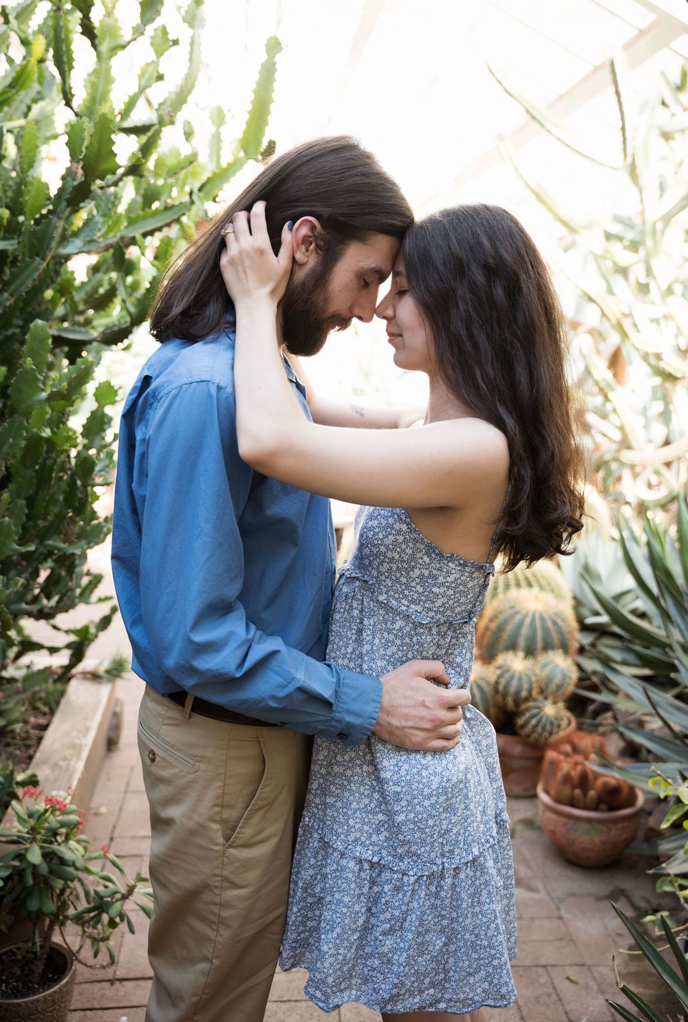 Romantic couple embraces tenderly in a garden setting with cacti and greenery in the background.