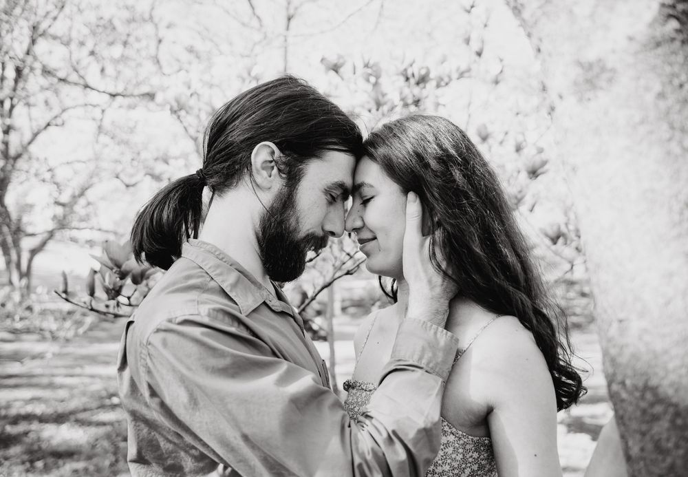 A romantic black and white photograph of a couple sharing an intimate moment outdoors among trees.