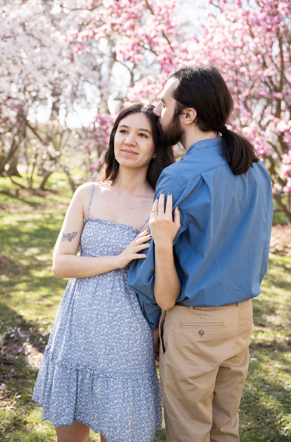 A couple embraces under blooming cherry blossom trees on a sunny spring day.