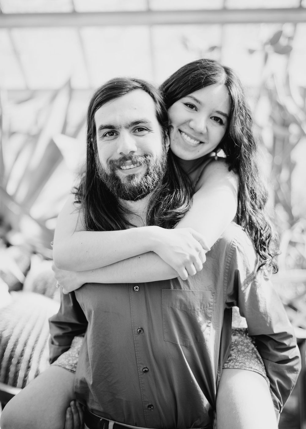 Black and white portrait of a smiling couple embracing outdoors, with long dark hair and casual attire.