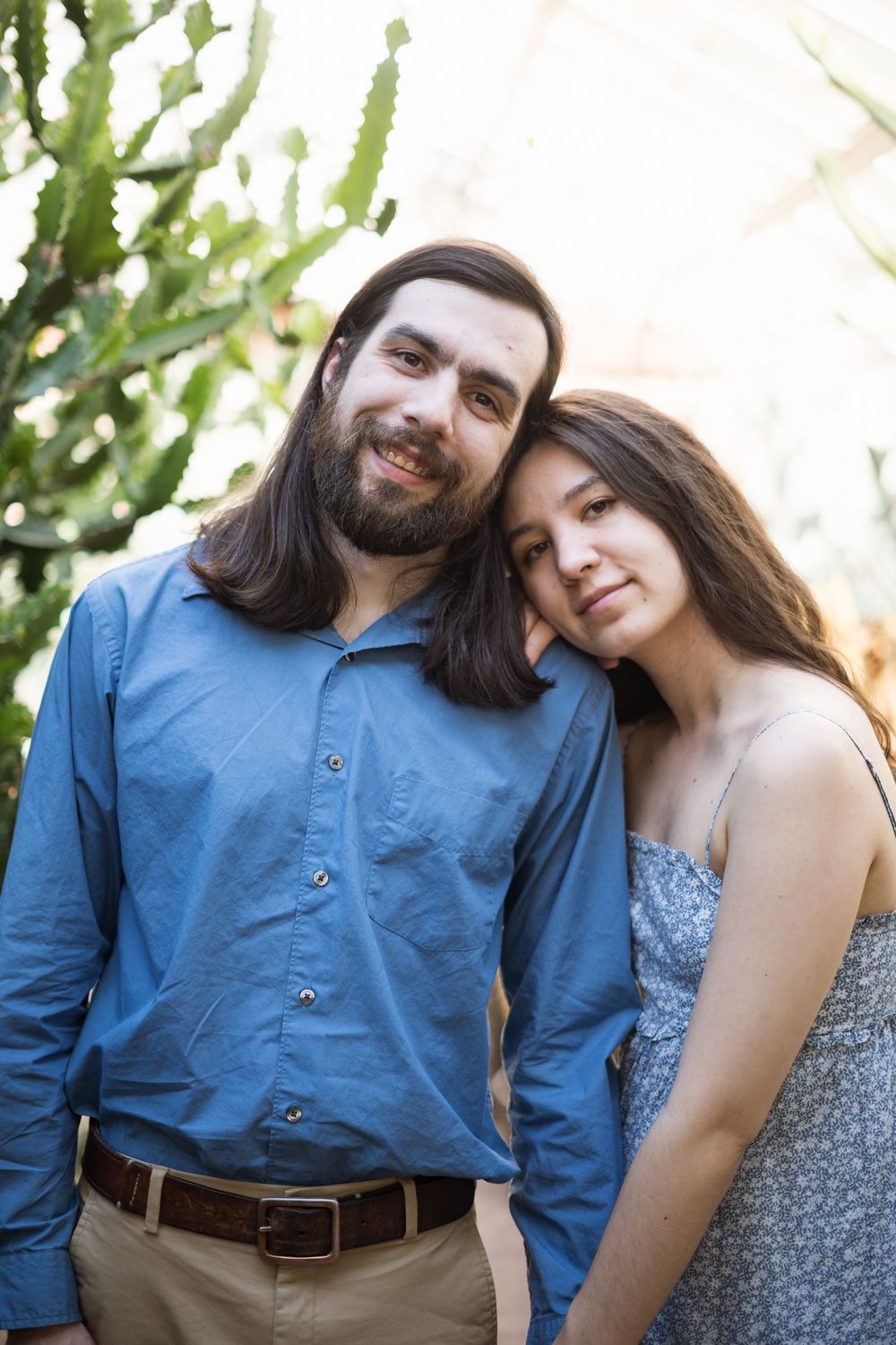A couple dressed in blue and floral print standing together outdoors with cacti plants in the background.