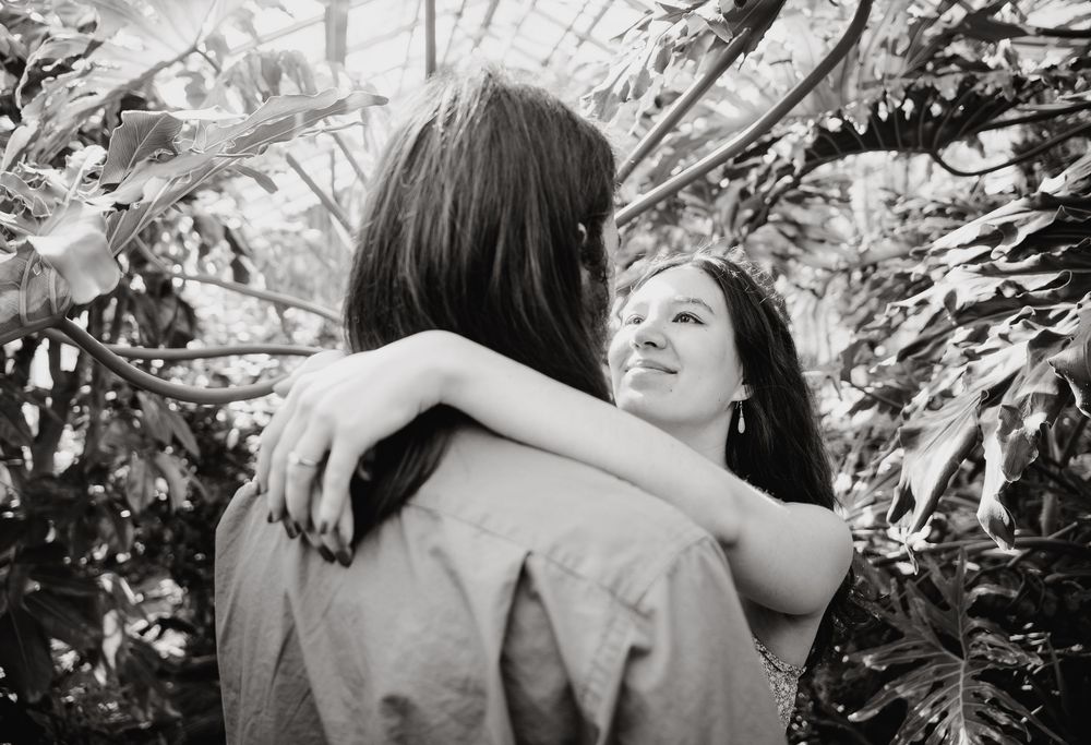 A tender black and white embrace is captured outdoors with leaves and foliage in the background.