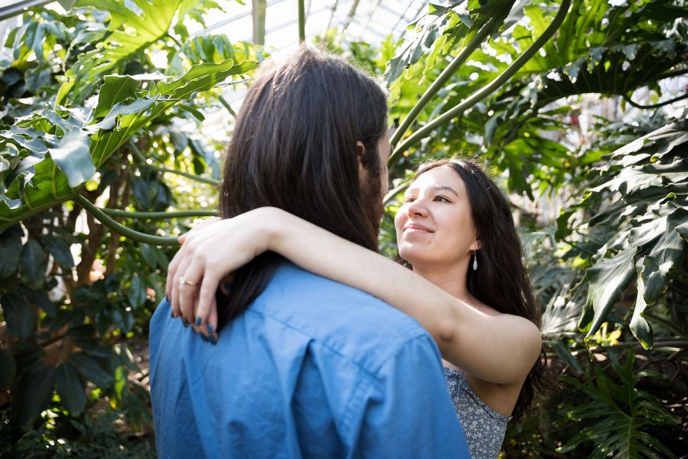 A couple embraces warmly in a lush tropical garden setting with green foliage surrounding them.