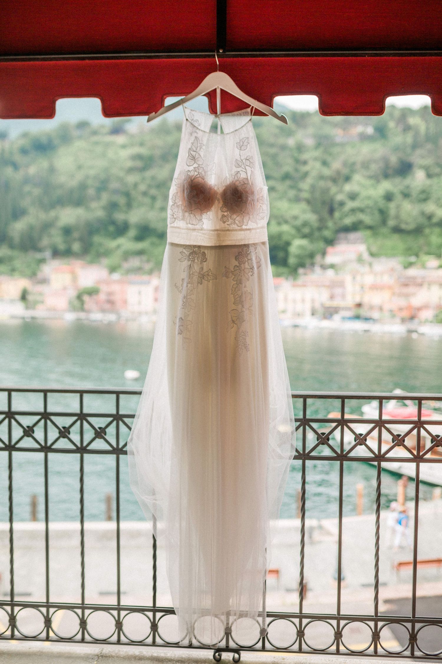 An elegant white lace wedding dress hangs on a balcony overlooking lake Garda Italy Hayley Elizabeth photography