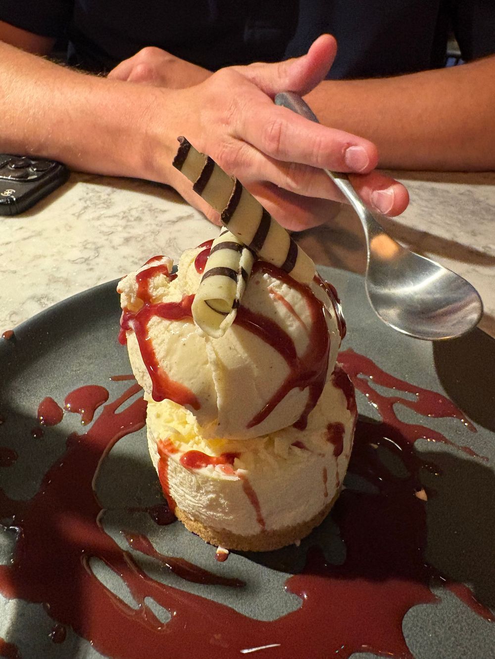 A dessert of vanilla ice cream topped with chocolate drizzle and a decorative chocolate pirouette wafer served on a dark plate.