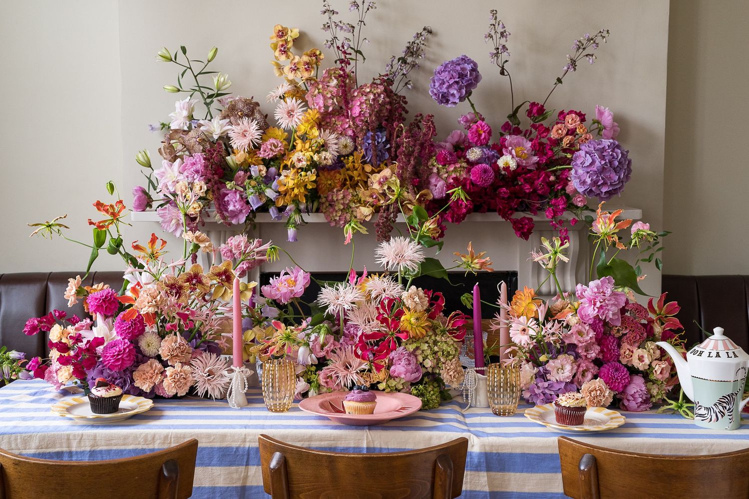 A lavish floral centerpiece arrangement in purple, pink and orange hues adorns an elegant table setting with teacups and glassware.