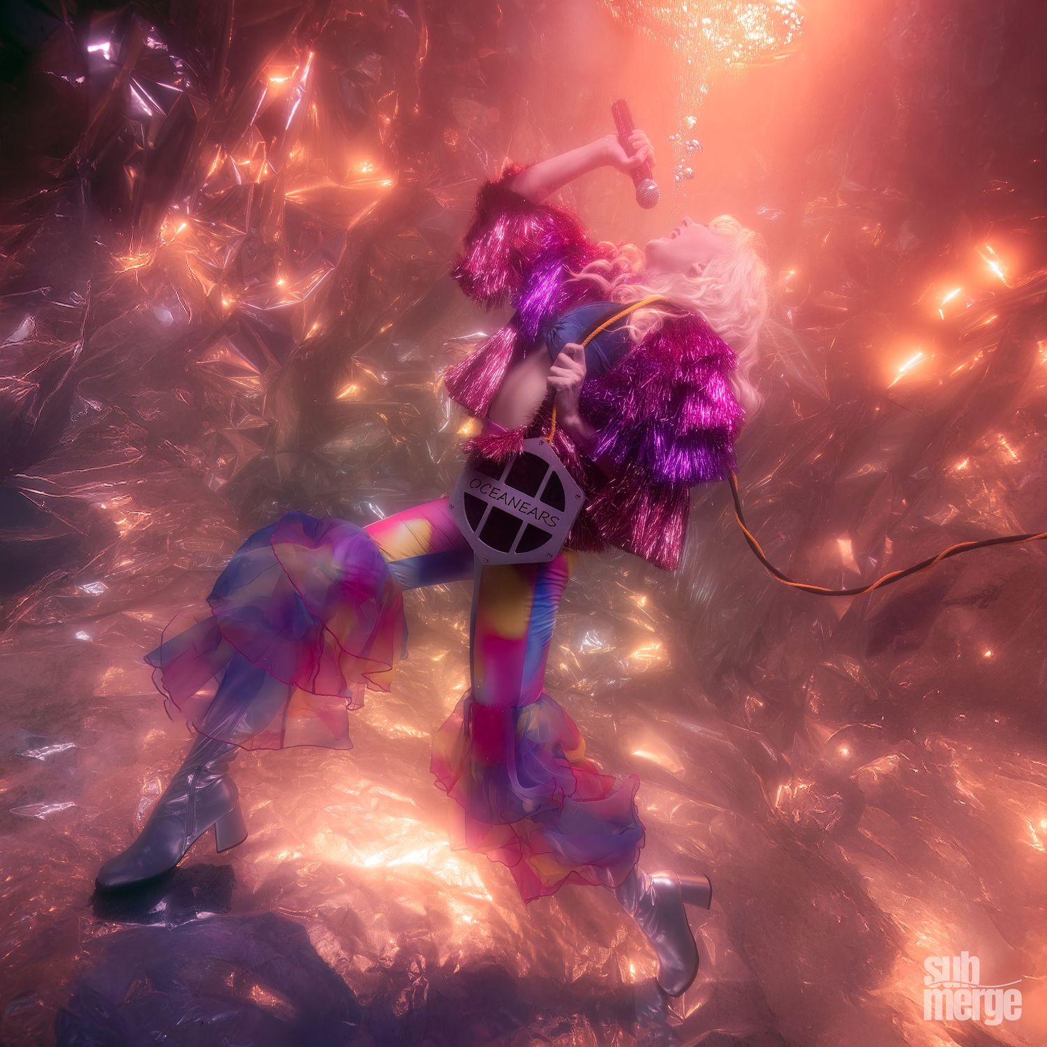 Underwater photographer captures a futuristic performer in a neon purple outfit dancing against a sparkly red illuminated background with dr