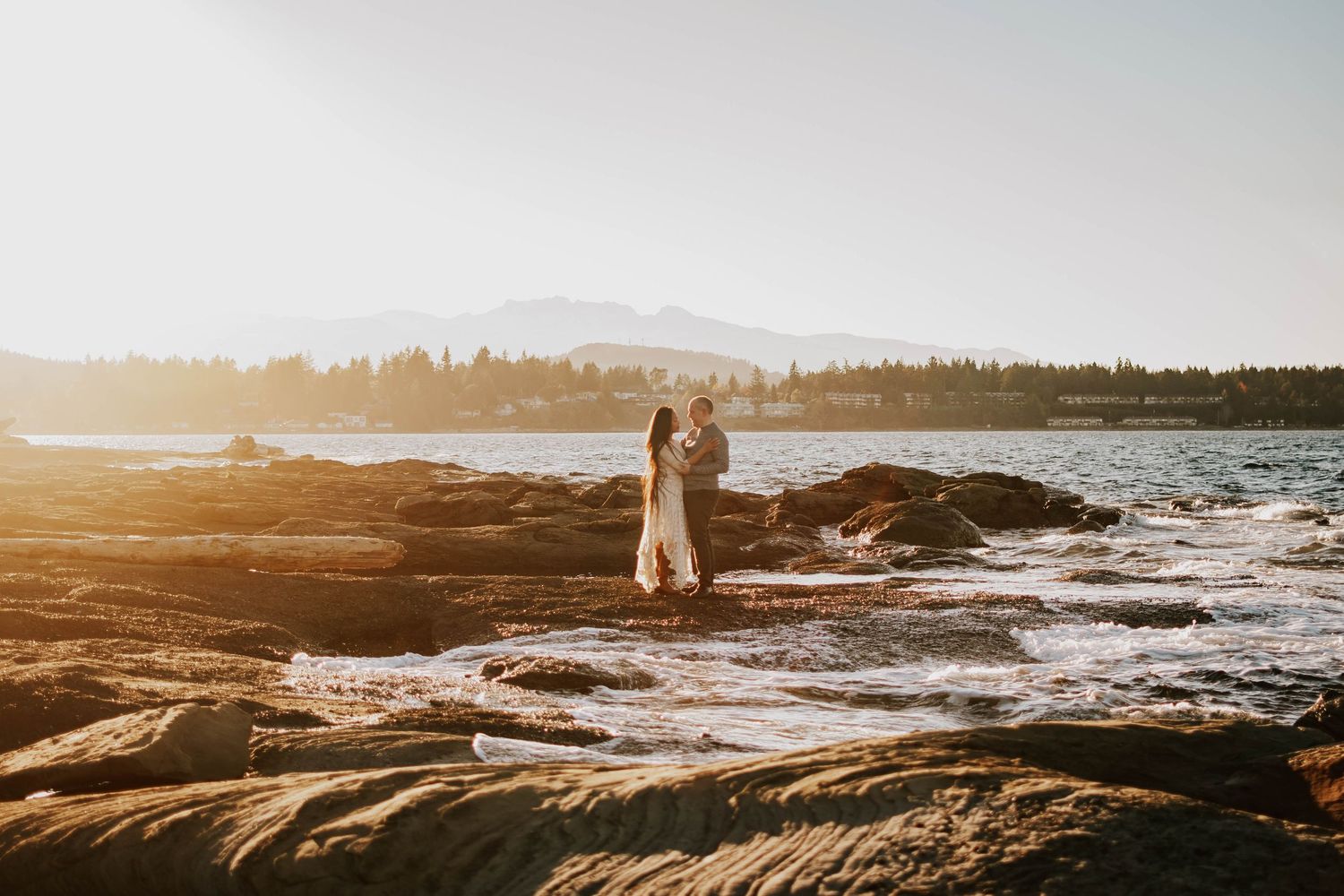 Beautiful photography of couple holding hands and embracing along Madrona Point beach's rocky shore on Vancouver Island during golden hour