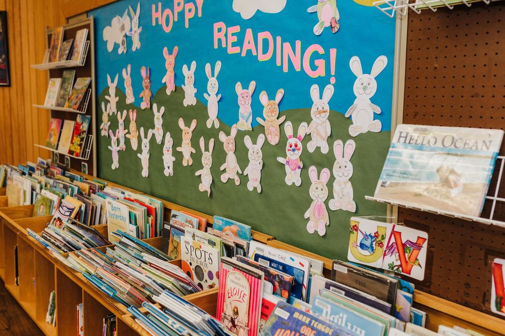 Children's library bulletin board featuring hop hop reading theme with white paper bunnies against blue sky background.