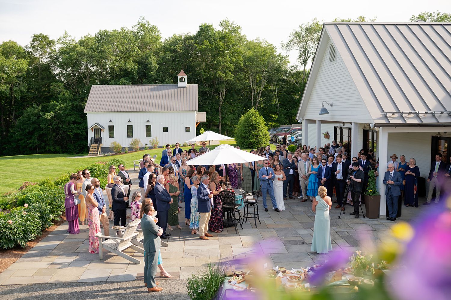 Wedding celebration with guests gathered outside a white church and reception venue on a sunny summer day.