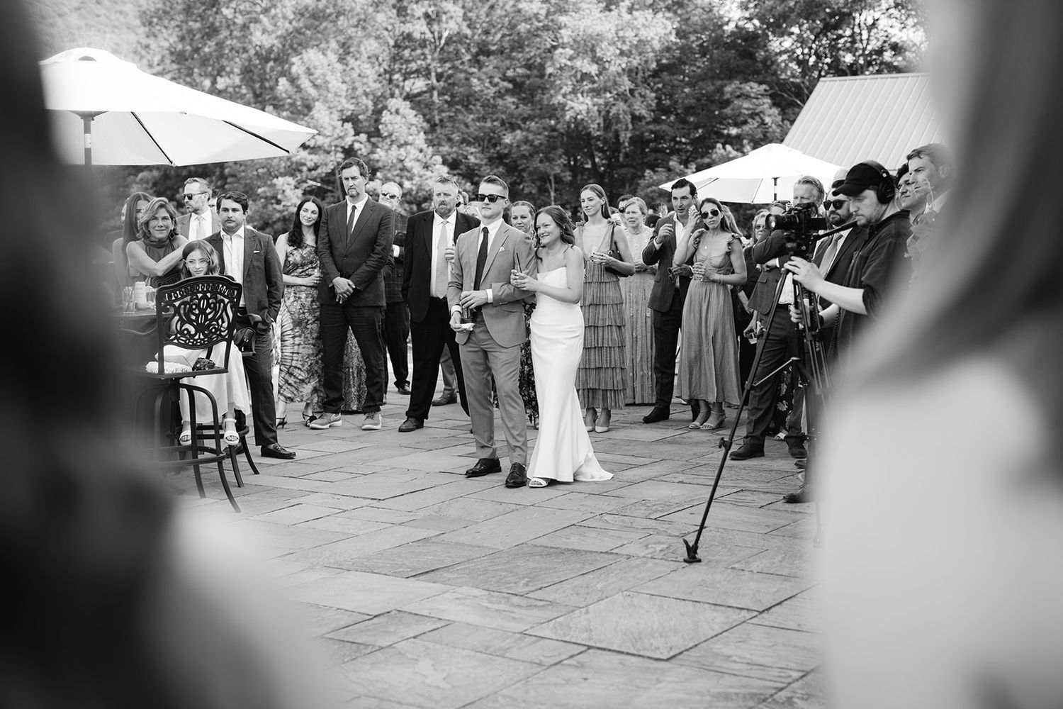 Black and white wedding scene shows guests dancing and celebrating in an outdoor patio setting.