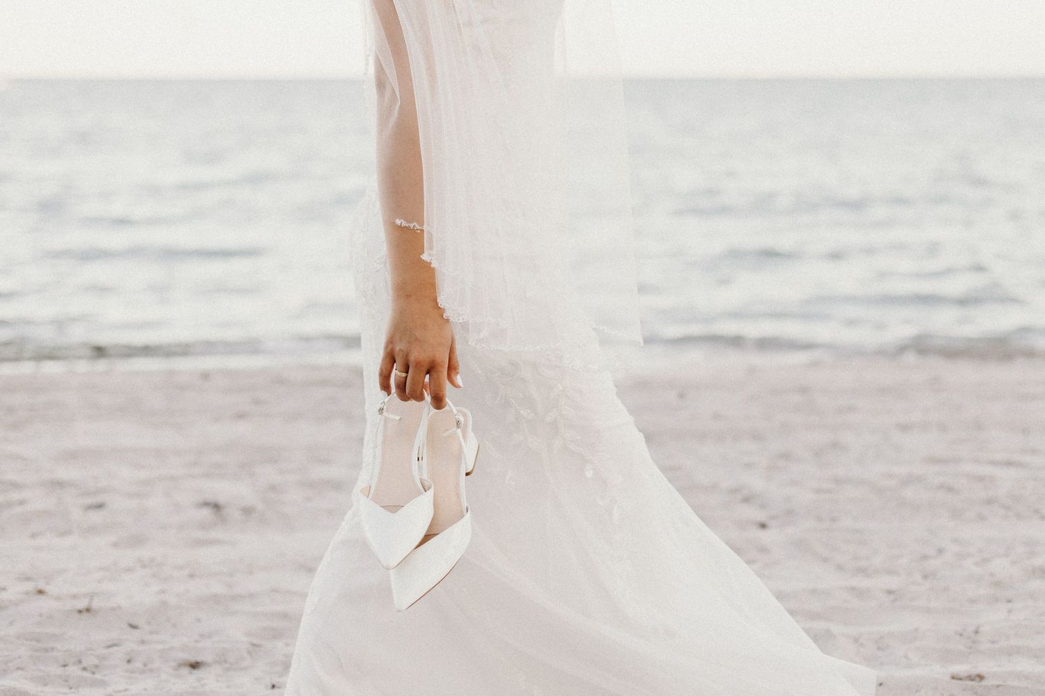 An elegant fashion photo of a figure in a flowing white gown posing against draped fabric in dramatic lighting.