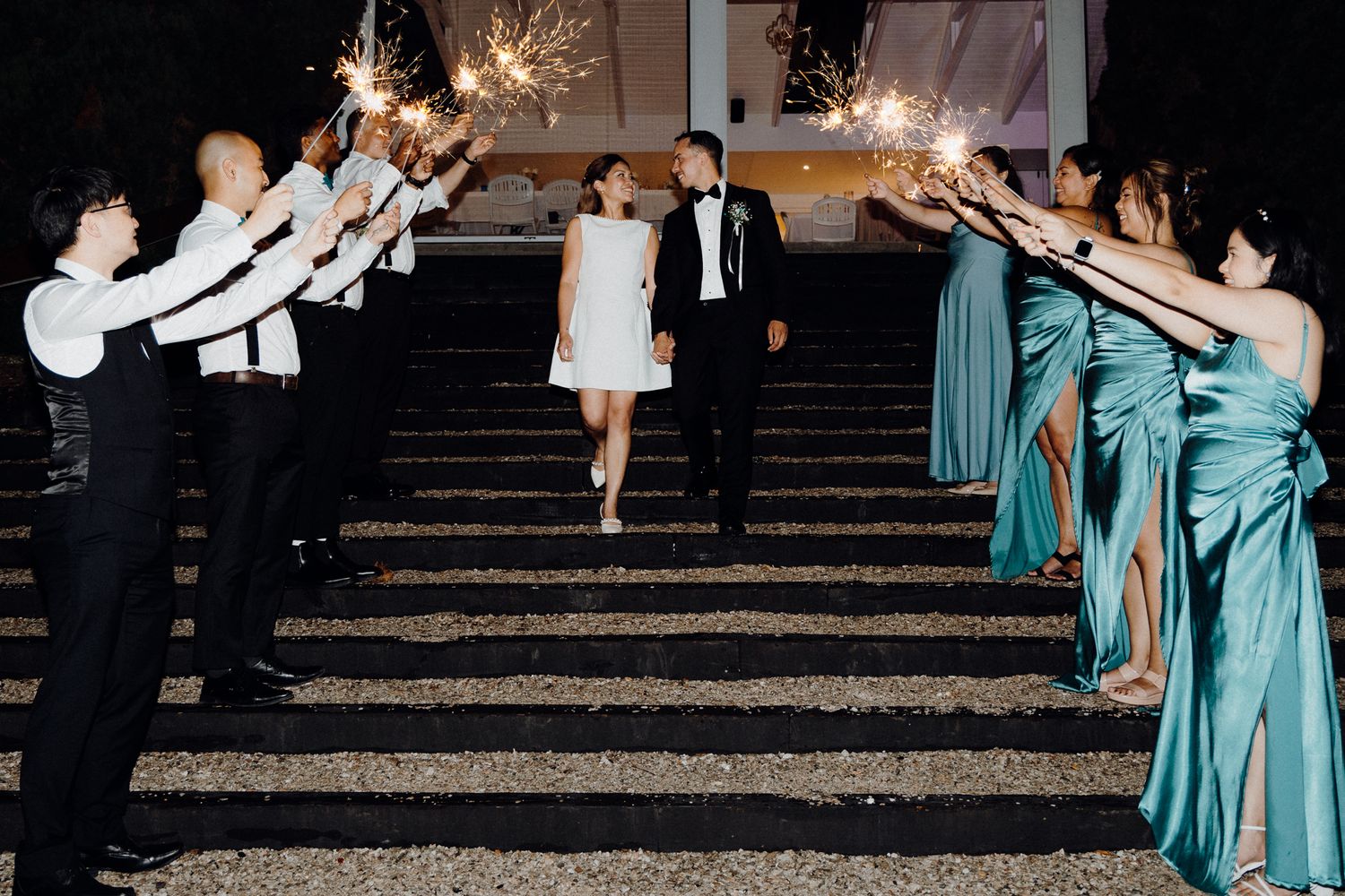 Wedding party members hold sparklers forming an archway as couple exits captured by Apertured Media Auckland Wedding Photographer.