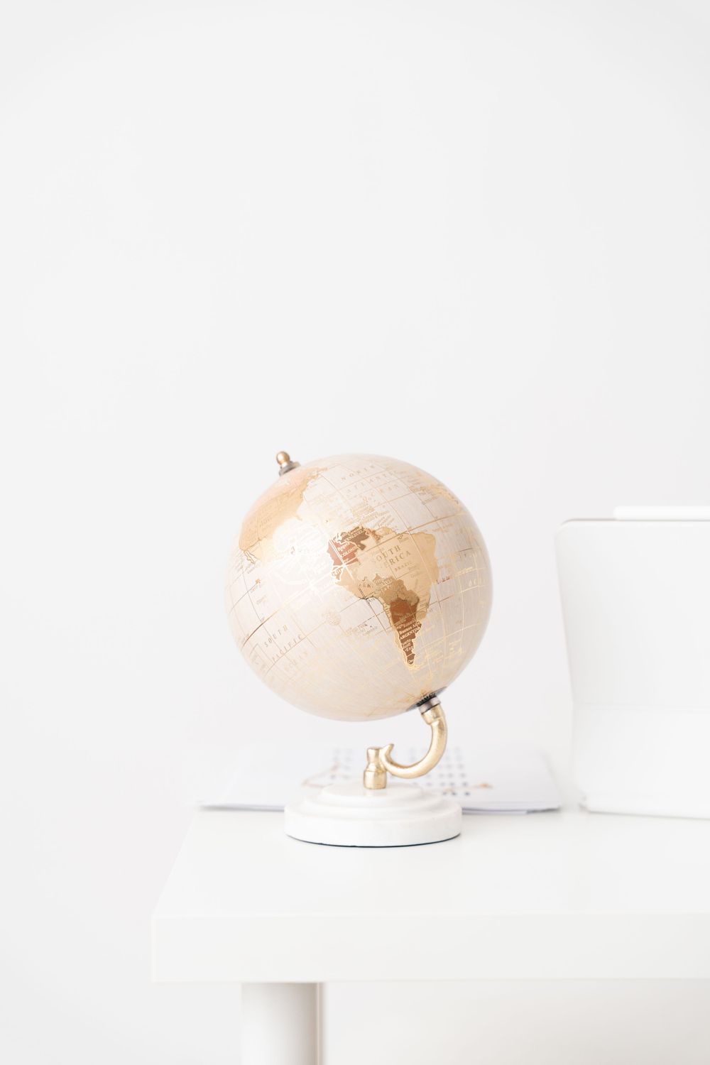 Small decorative cream and gold globe on white stand against minimal white background.