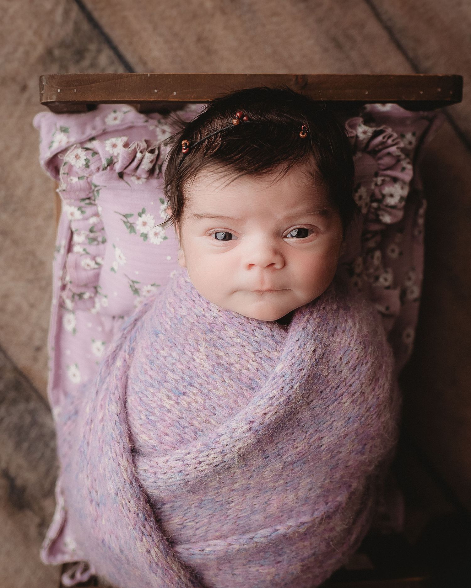 professional photo of a newborn baby wrapped in purple laying on a bed