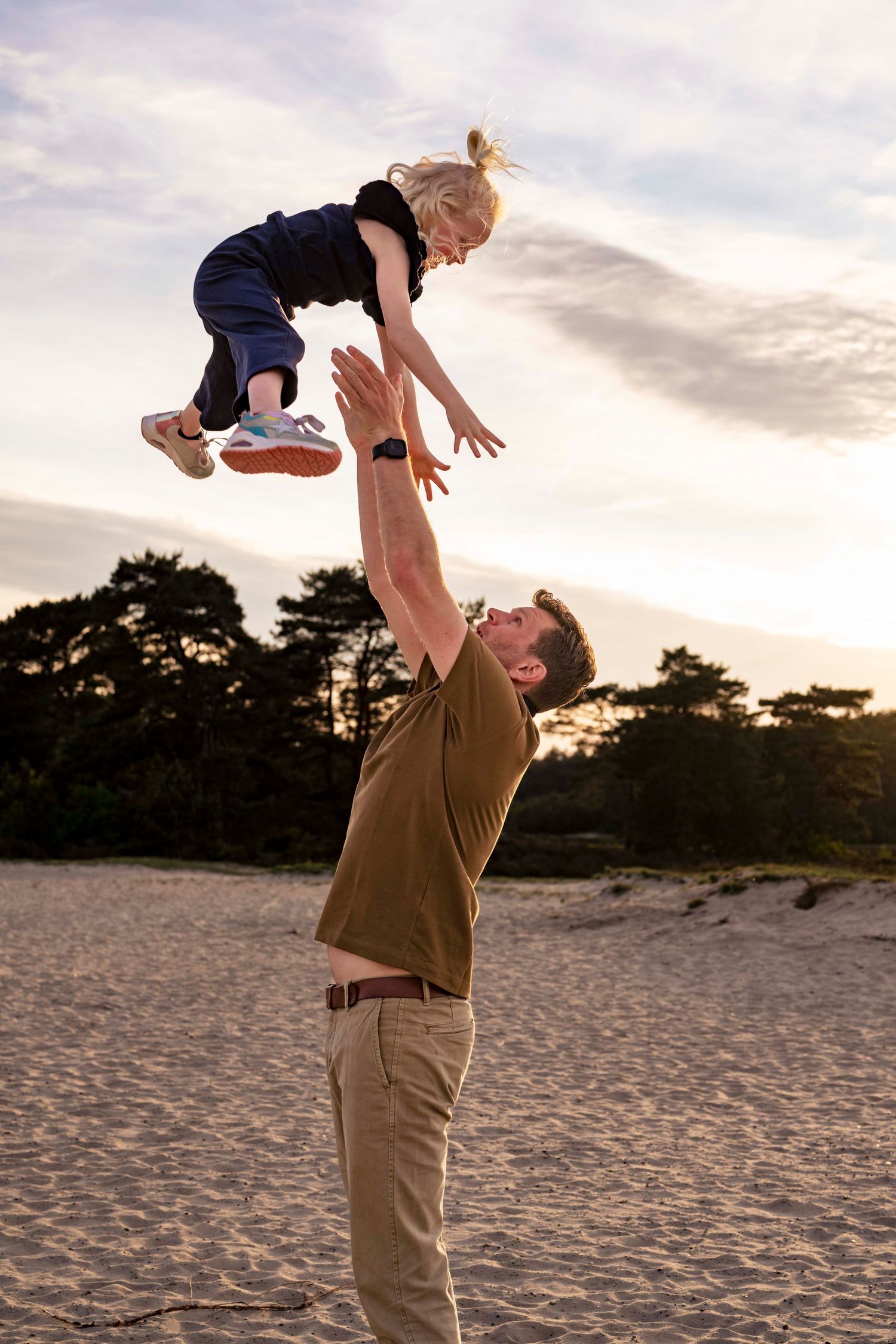 Playful beach scene with figure tossing child high in the air at sunset.