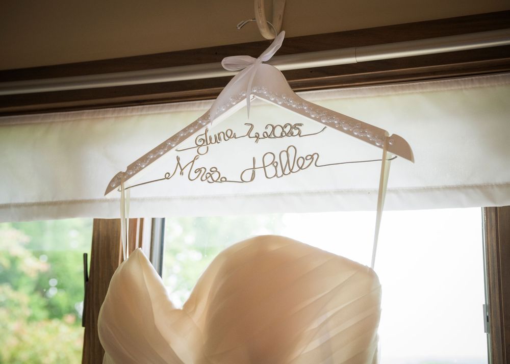 White wedding dress hanging on custom personalized hanger against wooden backdrop.