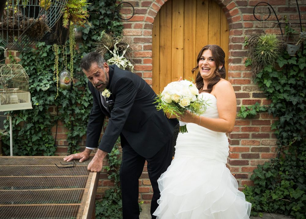 A wedding couple sharing a lighthearted moment on brick steps outside a wooden door.