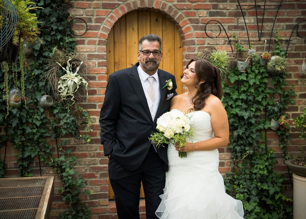 Wedding couple poses in front of rustic brick archway with wooden door and climbing ivy.