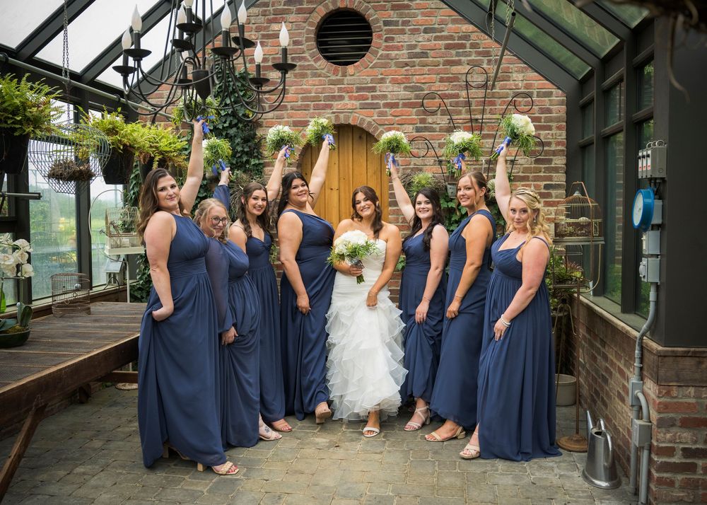 Bridal party in navy blue dresses gathers around bride for photo in brick courtyard.