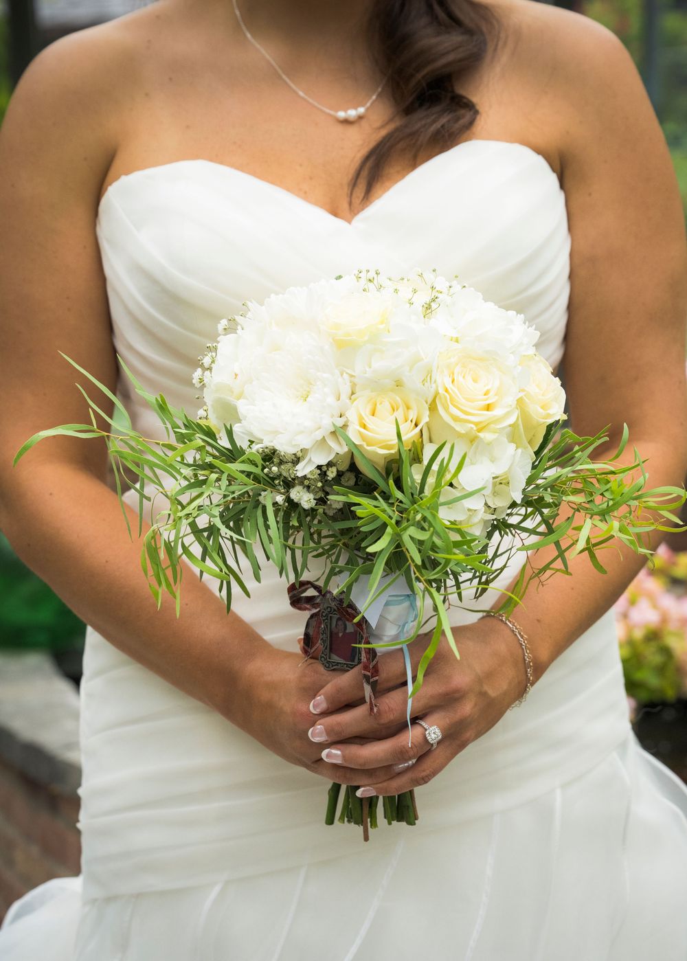A classic white bridal bouquet featuring roses and greenery held against a wedding dress.