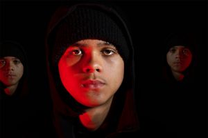 Dramatic portrait lit by red light showing figures in black beanies against dark background.