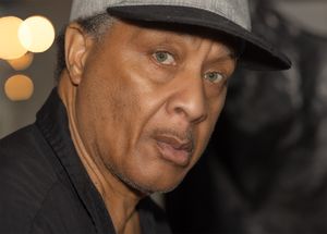 Person wearing a black cap and shirt at night with bokeh lights in the background.
