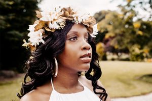 Portrait wearing a delicate floral crown of white and peach blooms against a natural outdoor setting.