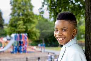 Bright smile at a playground with colorful play equipment visible in the background.