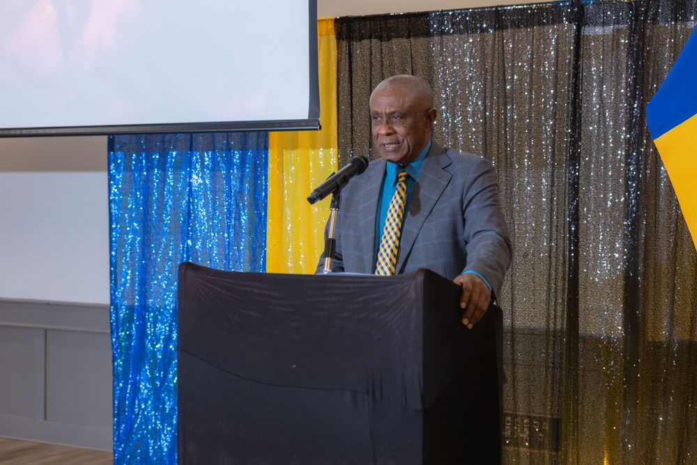 A speaker presenting at a podium with blue and yellow backdrop decorations.
