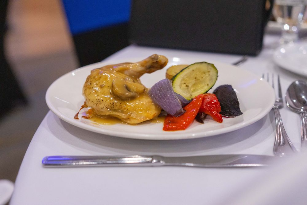 A plated dinner with roasted chicken, vegetables and garnish on elegant white dinnerware.