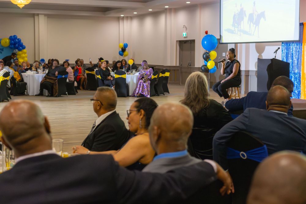 An audience watching a presentation in a banquet hall with blue and yellow balloons.