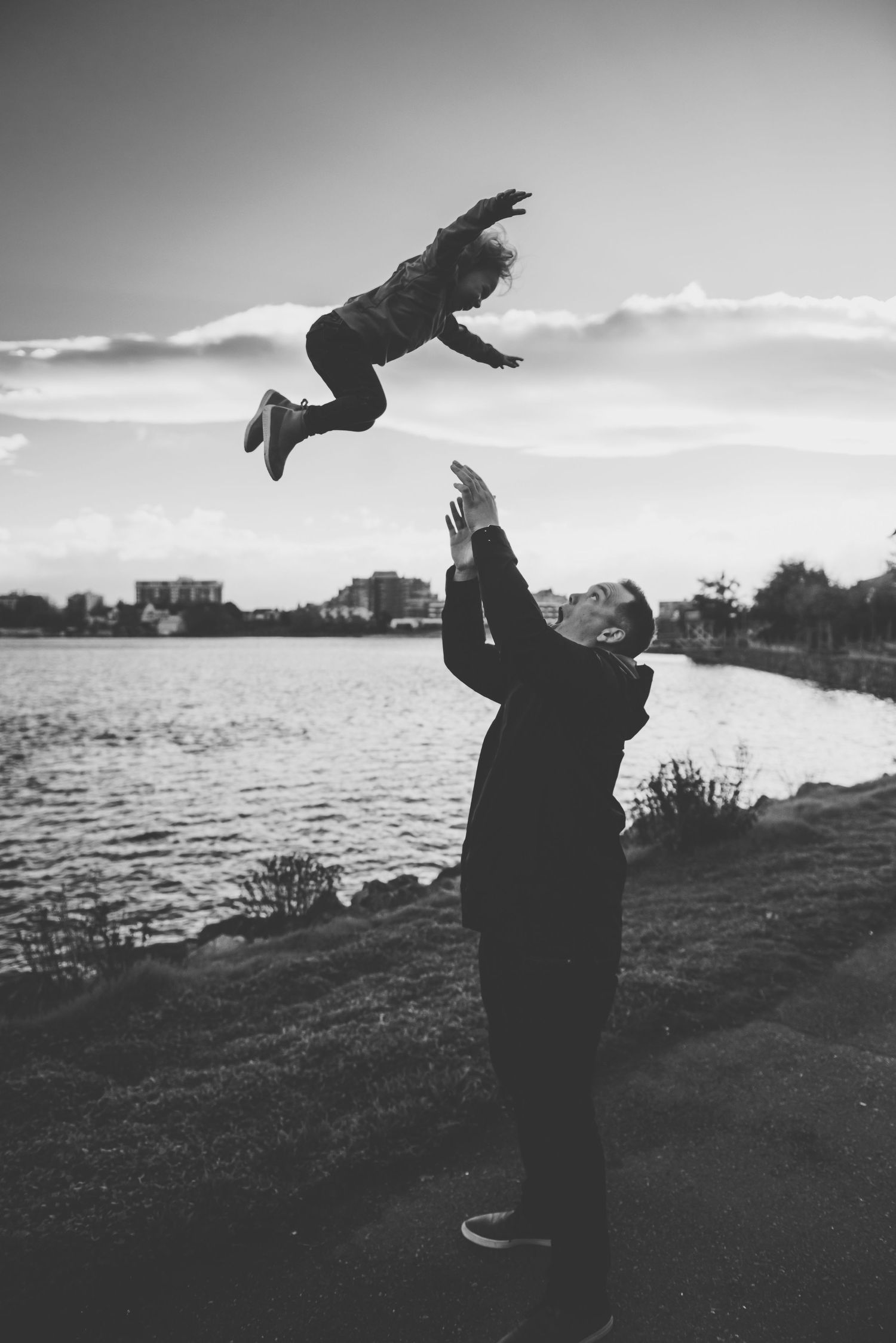 A joyful moment as a father tosses his child high into the air by the water, capturing a scene of trust and playfulness