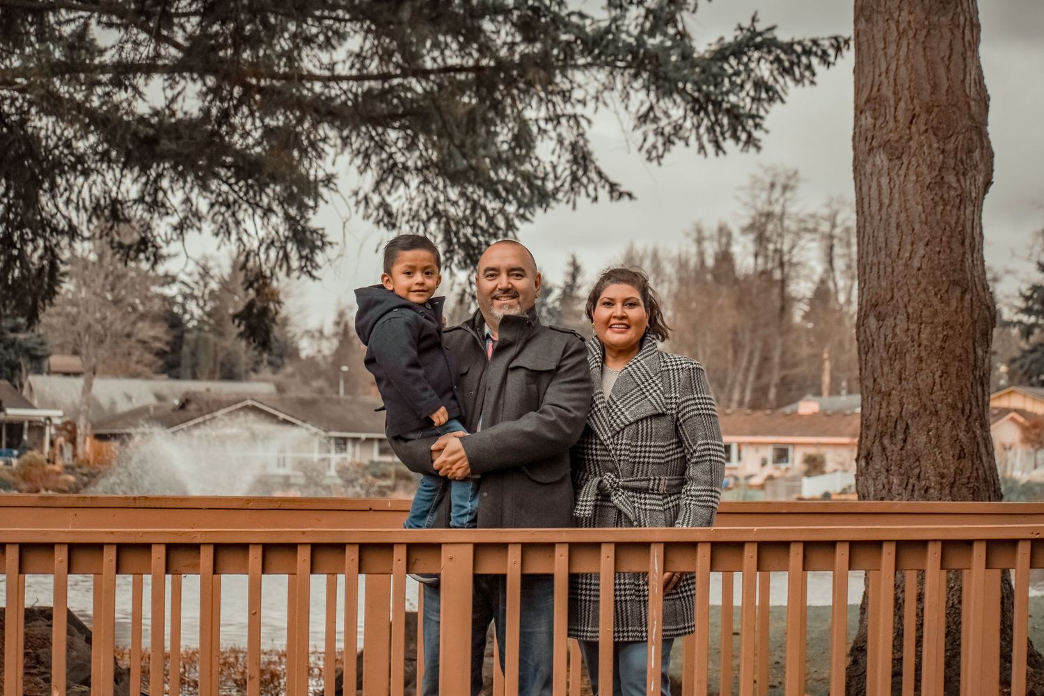 Family posing together on wooden deck with trees and houses in background.