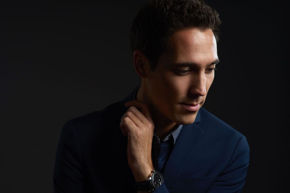 Bastien Baumet in a dark navy suit poses against a black background in dramatic low-key lighting photographed by Evan Will of Sharko Studios