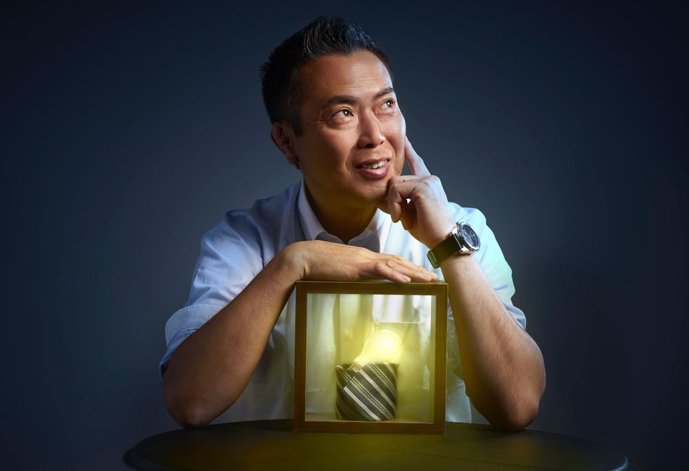 Hiromi Kojima smiling while leaning on a glowing yellow wooden box against dark backdrop photographed by Evan Will of Sharko Studios
