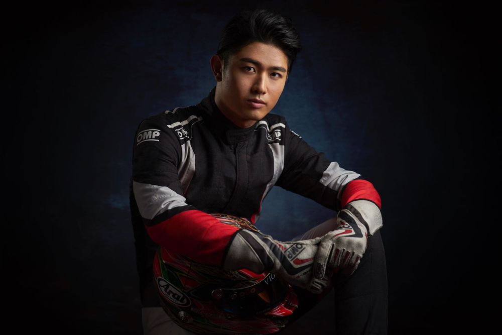 Yu Kanamaru in black and red motorsport gear poses confidently against dark background in dramatic lighting photographed by Evan Will