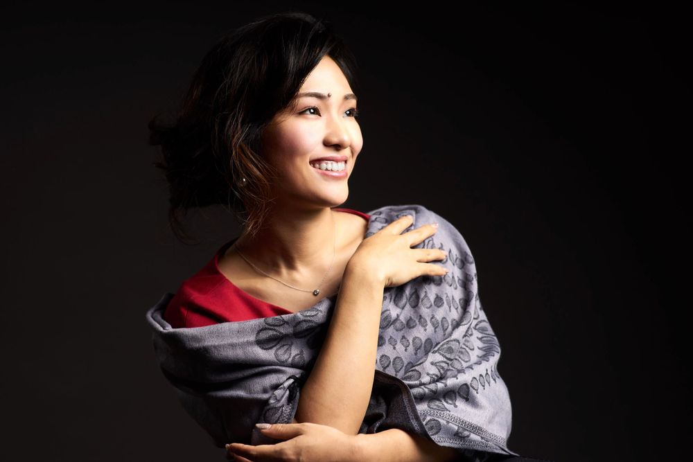 Yurina Omuro wearing a grey silk wrap poses against dark background with dramatic lighting while smiling warmly photographed by Evan Will
