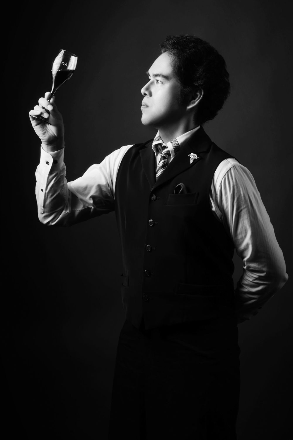 Dramatic black and white portrait of a sommelier in a vest and tie examining a small object in dramatic lighting photographed by Evan Will