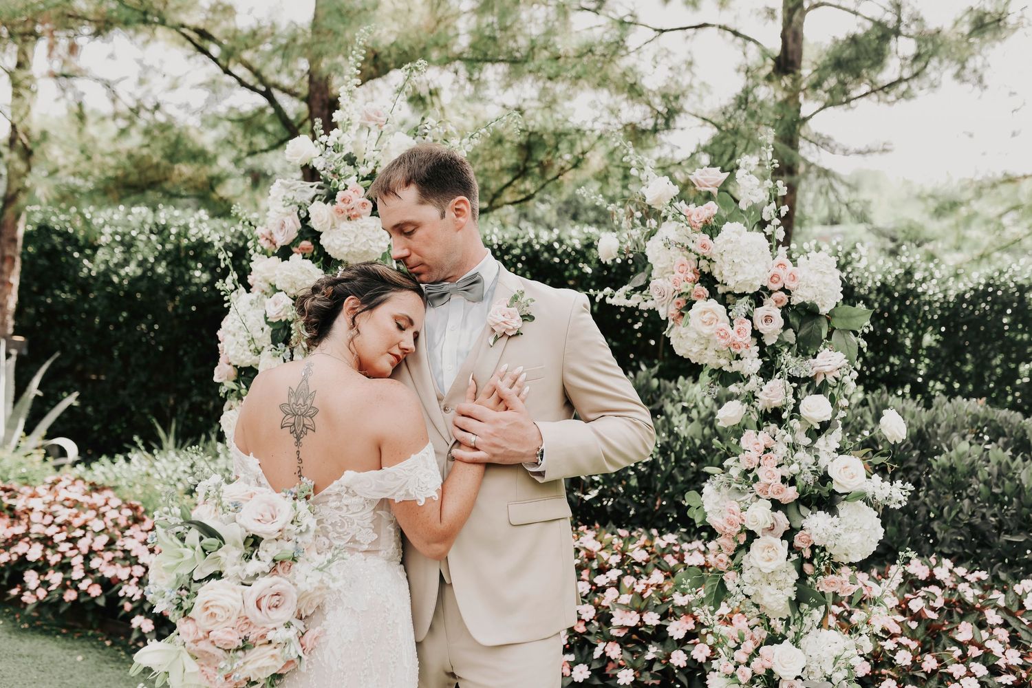 caroline wrests her head on her husband's shoulder surrounded by blush and ivory florals and greenery