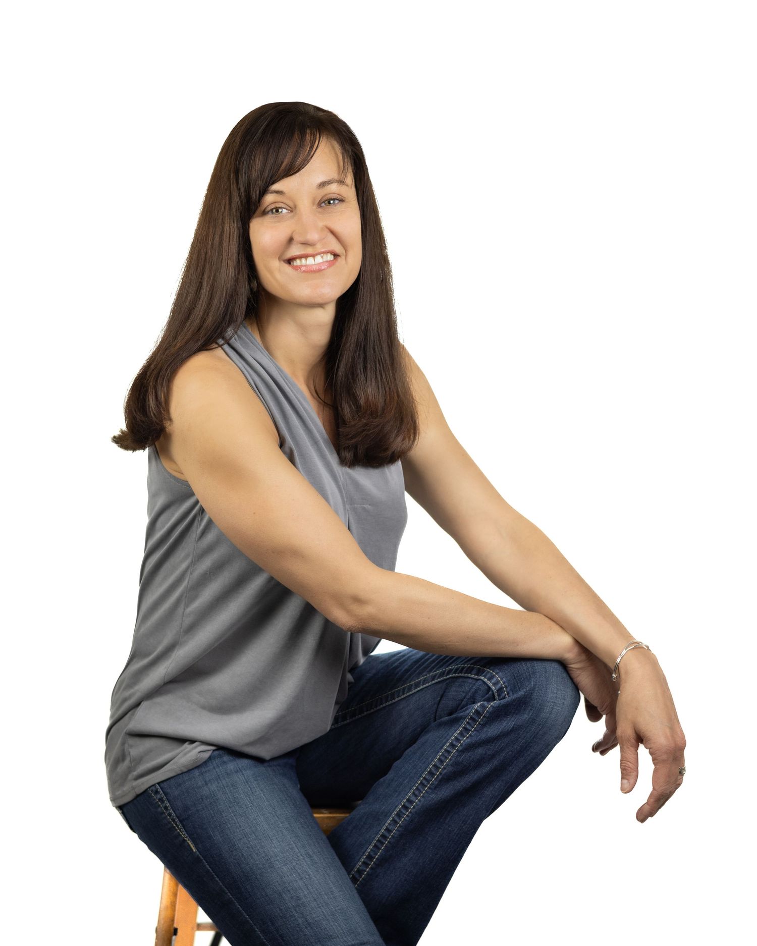 Person in gray sleeveless top and jeans sitting on floor in warm lighting with casual relaxed poses.