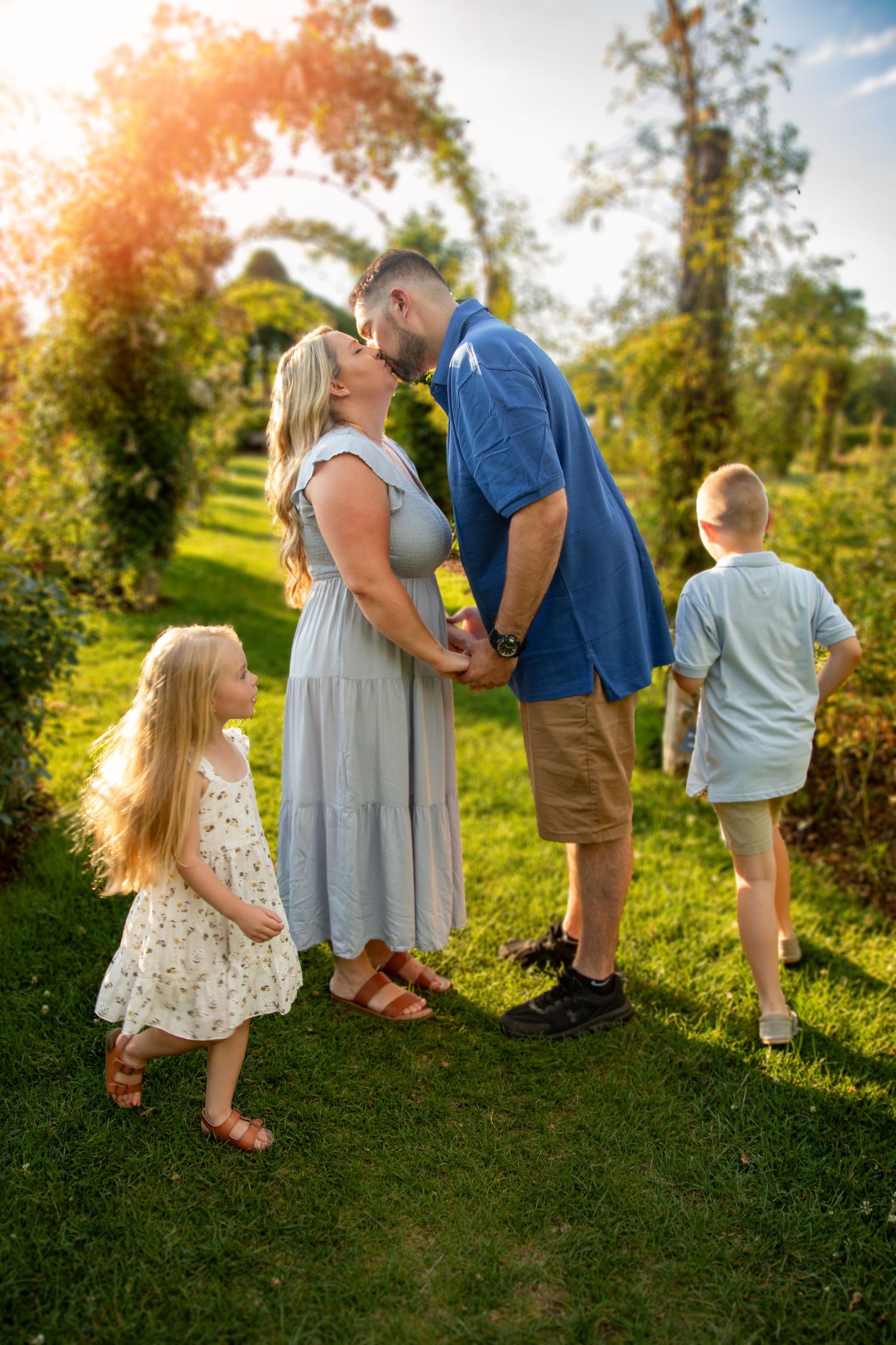 A loving family shares a tender moment in a sunlit garden during golden hour as two children watch nearby.