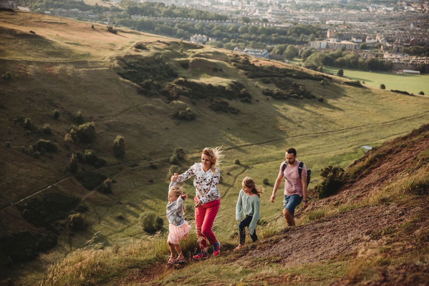 A winding dirt trail on a hillside overlooking a coastal city with bare trees and blue skies above.