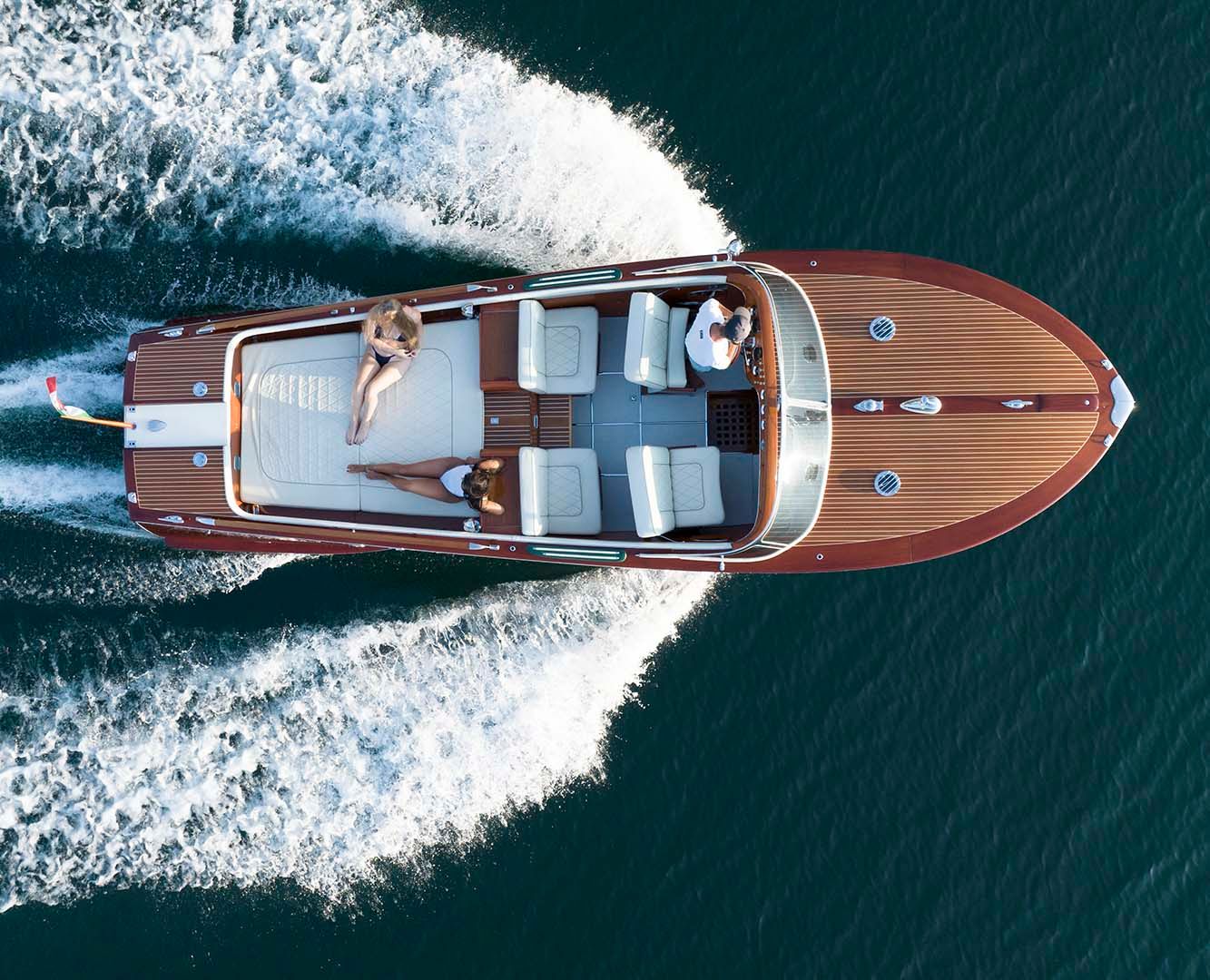 Aerial view of a classic wooden speedboat cruising through turquoise waters with a white wake trailing behind.