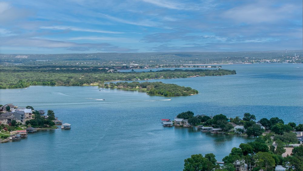 Aerial view of blue lake waters with green islands and shorelines under wispy clouds on a sunny day.