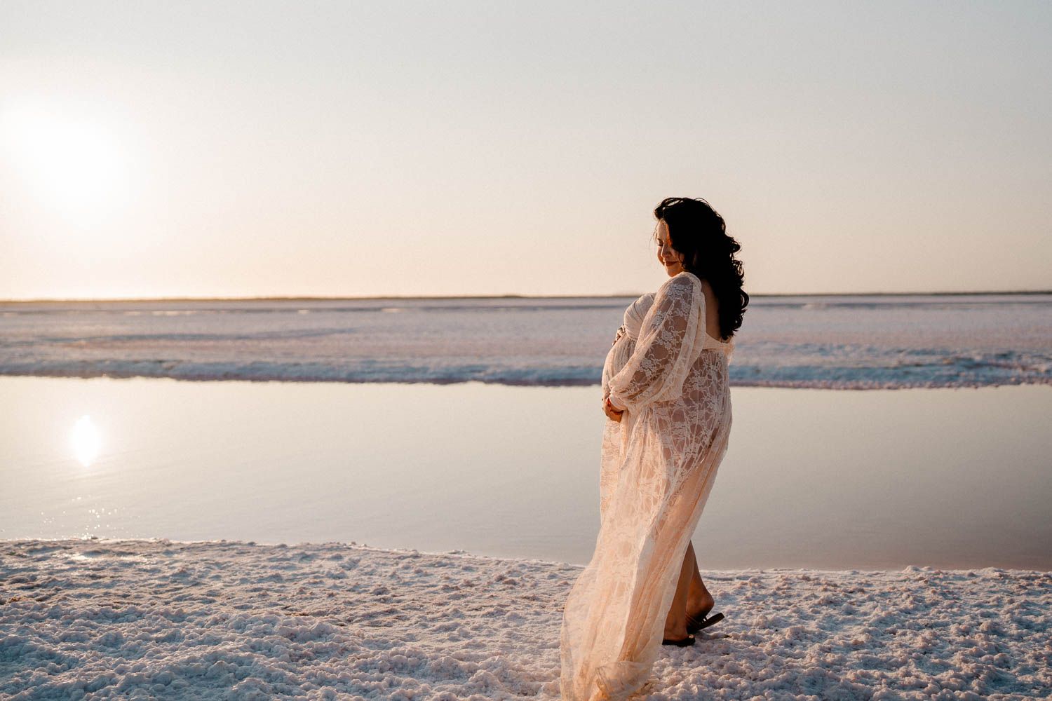A dreamy coastal scene with a white dress figure silhouetted against the soft evening sky at the ocean's edge.