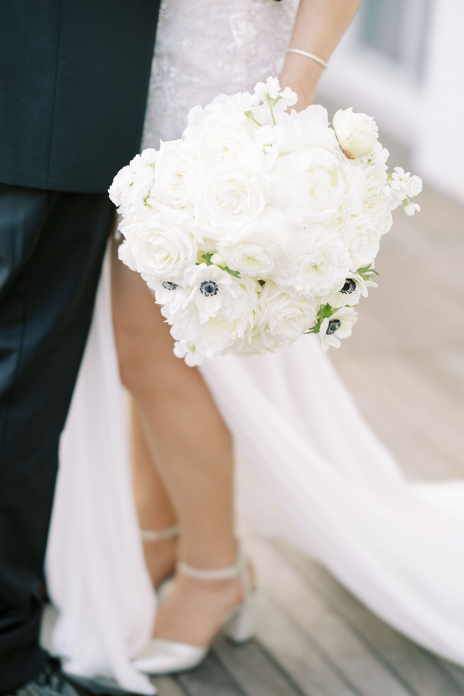 A delicate white floral bouquet featuring hydrangeas and anemone flowers held against a light background.