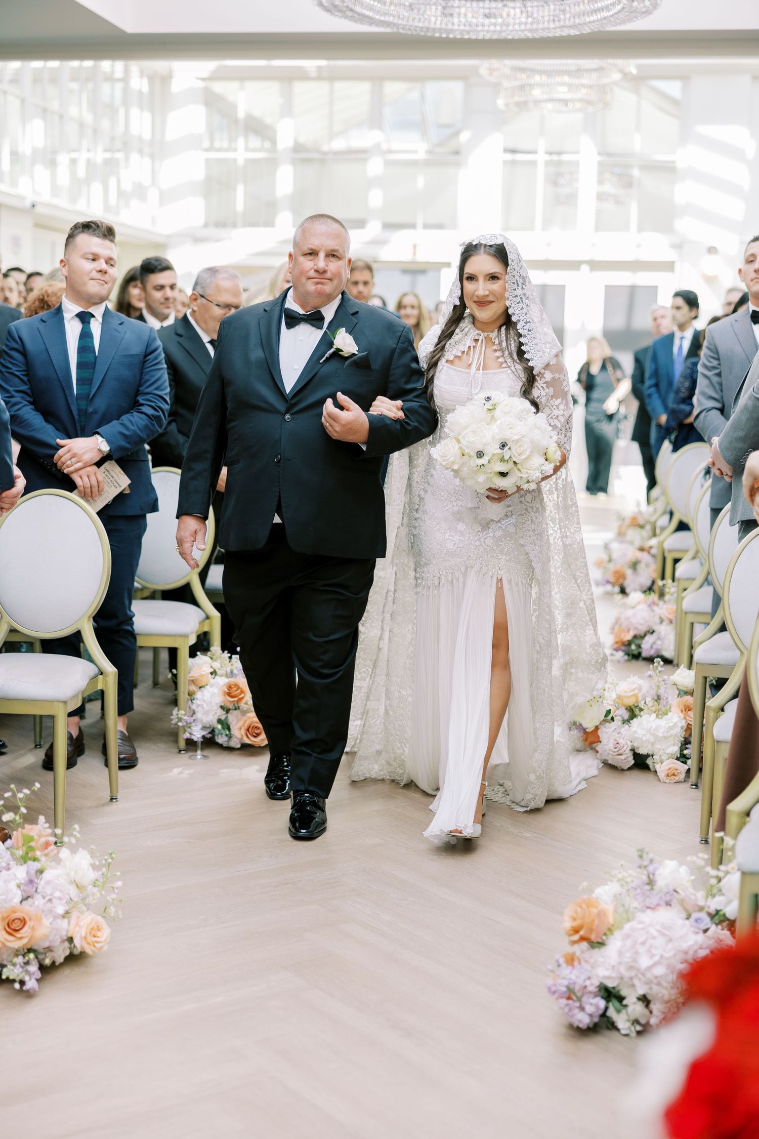 A traditional indoor wedding ceremony with floral aisle decorations and elegant gold chairs lining the walkway.